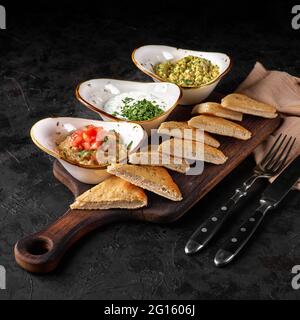 Set aus drei Arten von Dip-Saucen: Tzatziki, Guacamole, Auberginen-Kaviar auf rustikalem Holzbrett. Serviert mit arabischer traditioneller heißer Pita zum Dippen in Sa Stockfoto