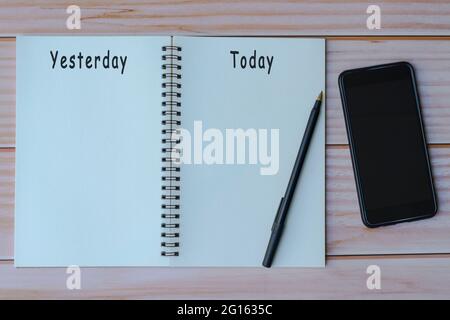 Gestern und heute auf Notizbuch mit Stift und Smartphone auf Holztisch geschrieben. Platz für Text. Flach liegend, Draufsicht Stockfoto