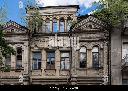 Die Fassade eines alten zerbröckelnden Hauses mit zerbrochenem Glas in den Fenstern und sprießenden Bäumen auf dem Dach. Spukhaus, altes, unheimliches Haus, Architekturrec Stockfoto