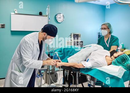 Männlicher Arzt mit Partner in medizinischer Uniform Vorbereitung weibliche Patientin in Sauerstoffmaske für die Operation im Krankenhaus Stockfoto