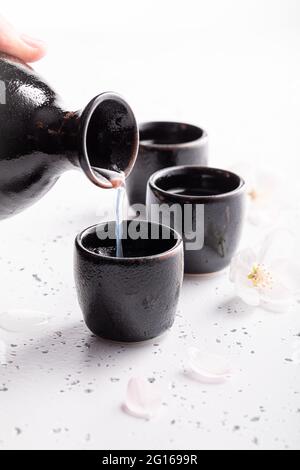 Starker Sake als traditioneller Alkohol. Japanische Gewohnheit, Alkohol zu trinken. Schwarze Keramik auf weißem Stein. Stockfoto