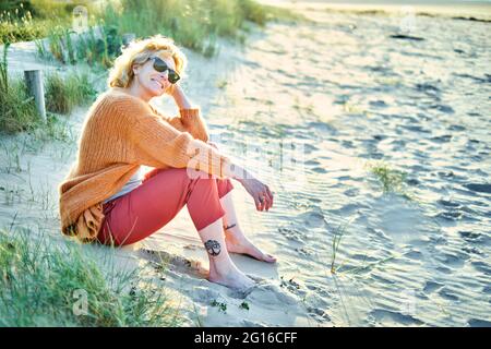 Junge reife blonde kaukasische Frau, die sich an einem sonnigen Tag an einem Strand entspannt. Stockfoto