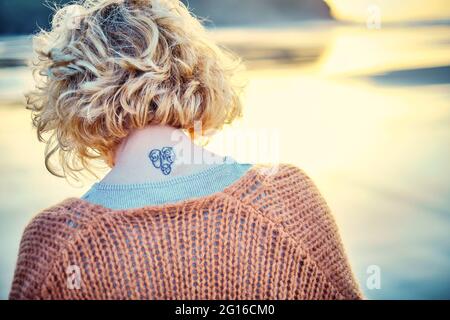 Rückansicht einer jungen blonden kaukasischen Frau mit einer Tätowierung in ist im Freien an einem Strand. Stockfoto