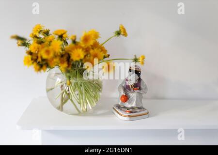 Ein Bouquet von Dandelionen in einer transparenten Glasvase. Figur eines Mädchens, das Tee gießt. Speicherplatz kopieren Stockfoto