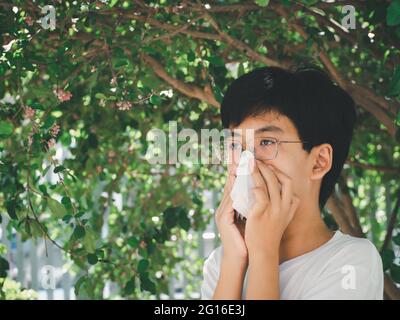 Kleiner Junge niest und bläst seine Nase, weil Pollenallergie aus der Nähe von Frühlingsbaum im Garten. Allergie cocnept. Stockfoto