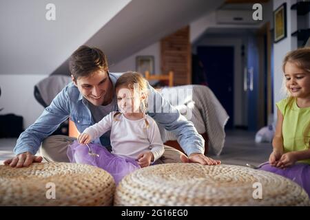 Ein junger Vater unterrichtete seine kleinen Töchter in heiterer Atmosphäre zu Hause beim Trommeln auf den Möbeln. Familie, zu Hause, spielen Stockfoto