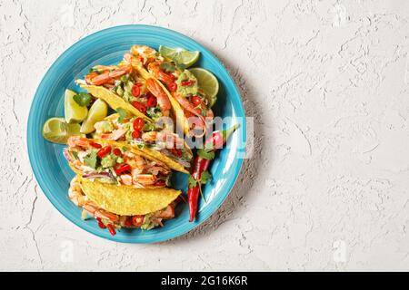 Garnelen-Tacos mit Kohlsalat, Limette und Guacamole auf einem blauen Teller auf einem weißen Tisch, flach liegend, freier Platz Stockfoto