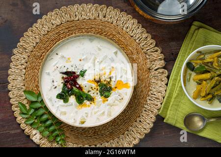 Pachadi oder Raitha und olan Kerala Festmahlgerichte, vegetarische Gerichte in einem Messinggefäß und einer weißen Schale, die auf einem Holzboden platziert ist Stockfoto