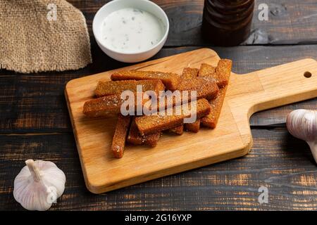 Roggenbrotcroutons, gesalzene knusprige Brotstäbchen auf Schneidebrett mit Knoblauch und Sauce Stockfoto