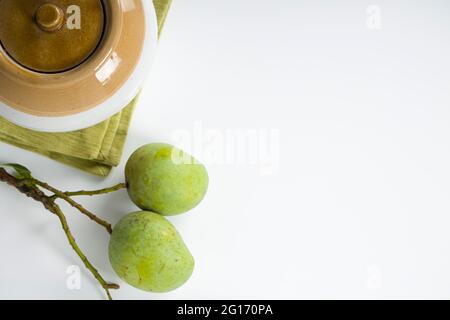 Rohes Mango und traditionelles indisches Gurkenglas, das auf weißem strukturiertem Hintergrund, selektivem Fokus und Draufsicht platziert ist. Stockfoto