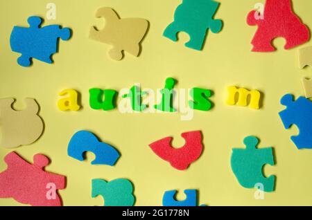 Das Wort Autismus aus farbigen Buchstaben mit Elementen eines mehrfarbigen Puzzles. Konzept des Welt-Autismus-Tages Stockfoto
