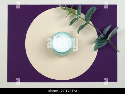 Draufsicht auf ein offenes Glas mit cremefarbenen und grünen Blättern auf farbigem Hintergrund. Beauty-Konzept mit kosmetischen Produkten für das Gesicht. Stockfoto