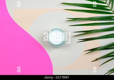 Draufsicht auf ein offenes Glas mit cremefarbenen und grünen Blättern auf farbigem Hintergrund. Beauty-Konzept mit kosmetischen Produkten für das Gesicht. Stockfoto