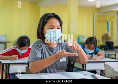 Asiatische Mädchen im Klassenzimmer trägt Gesichtsmasken und mit antiseptischen für Coronavirus Prävention. Die Grundschule ist bereit, nach Covid-19 Quar zu studieren Stockfoto