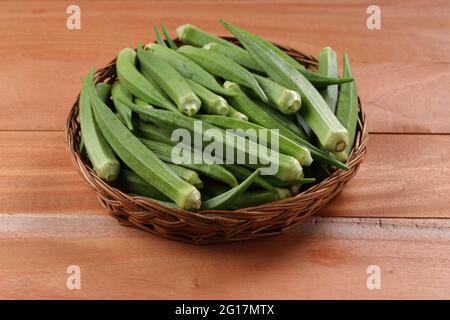 Okra oder Lady's Finger oder Bhindi frisches grünes Gemüse in einem Korb mit Holzstruktur Hintergrund angeordnet, isoliert und selektive Fokus Stockfoto