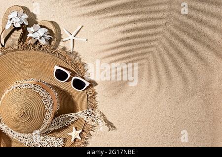 Braune runde Sommerhitze, weiße Sonnenbrillen, Sandalen und Seesterne mit Palmenblatt-Schatten auf Sand am Strand, Draufsicht, Kopierraum Stockfoto