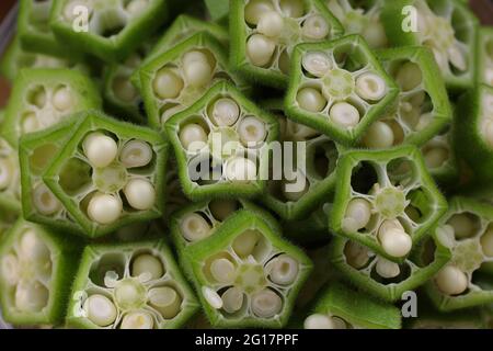 Okra oder Lady's Finger oder Bhindi frisches grünes Gemüse auf einem Holzbrett mit einer Glasschale voller Okra Scheiben Ringe mit Holzhintergrund angeordnet, Stockfoto