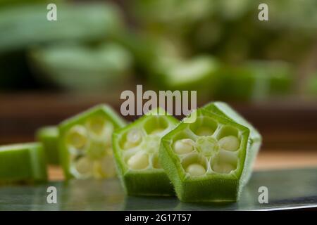 Okra oder Lady's Finger oder Bhindi, Nahaufnahme Bild von frischen grünen Gemüse geschnitten Ringe auf der Basis mit einigen Okra platziert dahinter angeordnet, selektiv Stockfoto