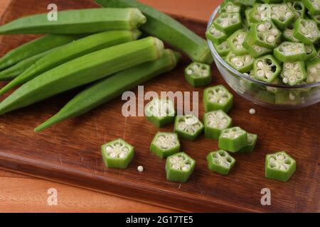 Okra oder Lady's Finger oder Bhindi frisches grünes Gemüse auf einem Schneidebrett mit einigen Scheiben in einer Glasschale platziert angeordnet, selektive Fokus. Stockfoto