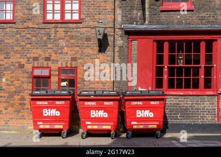 3 große rote Biffa Mülleimer an einer Ziegelwand mit roten Fenstern. London - 5. Juni 2021 Stockfoto
