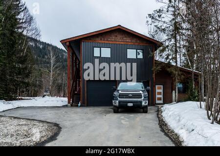 REVELSTOKE, KANADA - 14. MÄRZ 2021: Privathaus mit Auto in Kleinstadt Abendzeit früher Frühling mit Schnee Stockfoto
