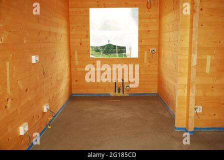 Ein Betonboden in einem neu gebauten Holzhaus (Tanne). Der blaue Schaum schützt Holz vor Beton. Wasserleitungen für das Waschbecken sind gegen die Wand. Udine, IT Stockfoto