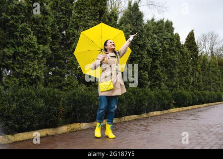 Glückliche ältere Frau, fröhliche ältere, ältere, pensionierte Frau mit gelbem Regenschirm, die das Leben an regnerischen Tagen im Park genießt. Genießen Sie jeden Moment, genießen Sie das Leben Stockfoto