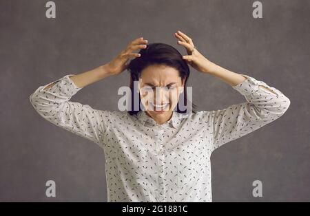 Emotional wütende Frau in Panik-Hysterie schreit und schreit auf einem Hintergrund von grauen Wänden. Stockfoto