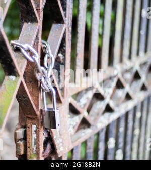 Konzentrieren Sie sich gezielt auf die Kette und das Vorhängeschloss, um den Zugang zu einem rostigen Metalltor mit geringer Schärfentiefe und Bokeh zu sichern Stockfoto