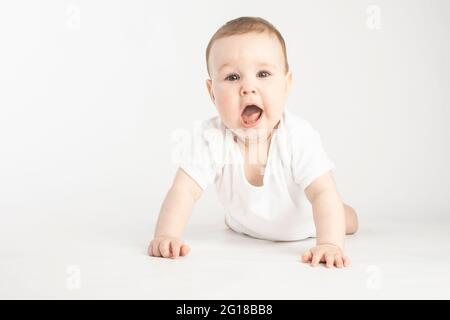 Überraschendes Baby, das in ihren Armen auf einem weißen Hintergrund steht. Stockfoto