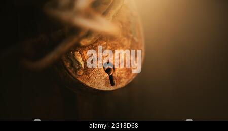 An einer Kette hängt ein rostiges altes großes Vintage-Schloss, das die alte Tür in der Halbdunkel schließt und von einem Lichtstrahl beleuchtet wird. Geheim. Stockfoto