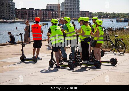 Eine Gruppe junger Menschen, die auf einer geführten Sightseeing-Tour mit Motorroller unterwegs sind, hält an einem Stadthafen in sonniger Sonne, sieht nach, reist und hält an Gebäuden. Kopenhagen, D Stockfoto