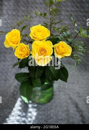 Schöne gelbe Rosen in einer grünen Vase stehen auf einer Decke. Überraschungs- und Urlaubskonzept Stockfoto