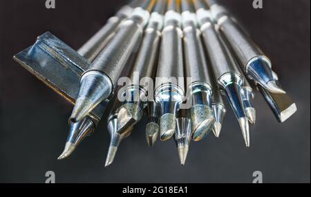 Satz Metallspitzen des Lötkolbens auf dunklem Hintergrund. Verschiedene Arten, Größen und Formen von gespiesten austauschbaren beheizte Arbeit Werkzeugbits in künstlerischen Detail. Stockfoto