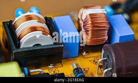 Nahaufnahme der Ringspule und der zylindrischen Spule auf der gelben Leiterplatte. Transformatoren, Kondensatoren und Dioden auf der Leiterplatte des Schaltnetzteils. Stockfoto