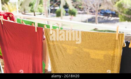 Bunte T-Shirts und andere Kleidungsstücke streckten sich auf mehreren Saiten auf einer Terrasse, die der Luft und der Sonne ausgesetzt war, um sie zu trocknen. Stockfoto