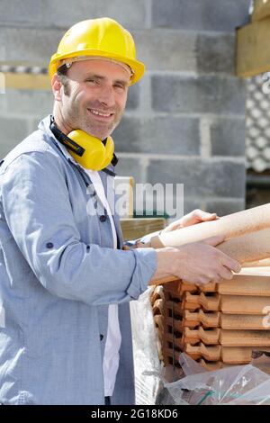 Arbeiter mit Helm, der Dachziegel hält Stockfoto