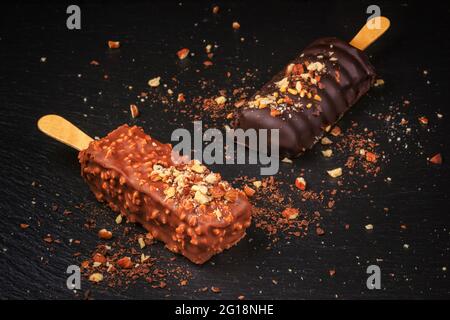 Schokoladenkuchen knallt mit Nüssen in Form von Popsicle auf Stick auf schwarzem Schiefertafel Hintergrund Stockfoto