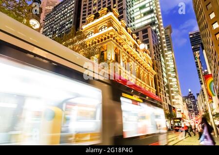 Die verschwommene Personenbahn entlang der George Street in der Innenstadt von Sydney überquert bei Sonnenuntergang den Martin Place - helle Lichter. Stockfoto