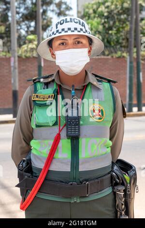 Vorderansicht mittellanges Porträt einer jungen und attraktiven peruanischen Polizistin mit einer OP-Maske in Lima, Peru während der COVID-19 Pandemie. Stockfoto