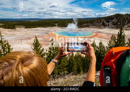 Grand Prismatic Spring im Yellowstone National Park, Wyoming, USA aus der Sicht des Fairy Falls Trail, mit einer Frau, die mit einem Smartphone ein Bild macht, Horizont Stockfoto