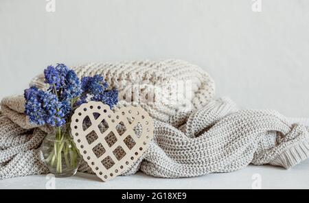 Warme Strickpullover in Pastellfarben, ein Bouquet aus Muscari-Blumen und ein dekoratives Holzherz. Stockfoto