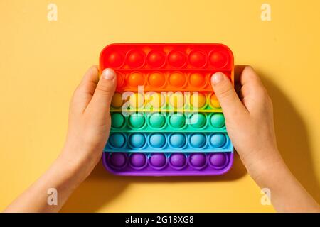 Die Hände eines Kindes drücken auf Pop-it-Spielzeug-Silikon auf einem gelben Hintergrund. Anti-Stress-Spielzeug, ein Trend bei Kinderspielzeug. Stockfoto