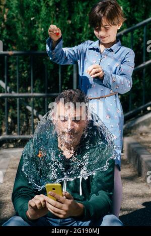 Mädchen sprengte einen mit Wasser gefüllten Ballon über den Kopf ihres Vaters Stockfoto