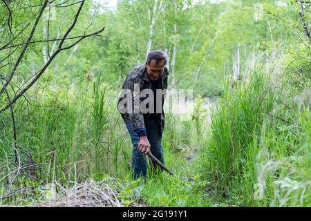 (210606) -- YICHUN, 6. Juni 2021 (Xinhua) -- Zhang Yingshan reinigt einen Bergpfad in einer Waldfarm, die vom Wumahe Forstbüro in der Stadt Yichun, nordöstlich der Provinz Heilongjiang, verwaltet wird, 3. Juni 2021. Zhang Yingshan, 65, arbeitet seit über 45 Jahren mit Bäumen. Nach dem Schritt seines Vaters wurde Zhang 1975 Forstarbeiter im Wumahe Forstamt. Neun Jahre später eröffnete er die erste familiengeführte Waldfarm des Büros, in der jedes Jahr 30 Hektar Bäume gepflanzt wurden. Von 1981 bis 2011 pflanzten Zhang und seine Frau Yan Yuping rund eine Million Bäume auf dem Stockfoto