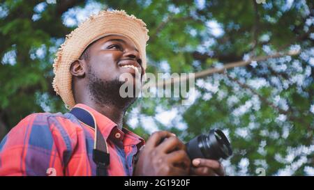 Afrikanischer Reisender Mann hält eine Kamera in der grünen Natur Bokeh Hintergrund Stockfoto