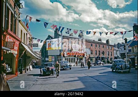 Auf der anderen Straßenseite gibt es farbenfrohe Strapazen, Gewerkschaftsflaggen und ein großes Schild mit einer Krone und den Worten ‘lang lebe die Königin’ in Surrey Street, Littlehampton, West Sussex, England, Großbritannien im Jahr 1953. Dies war für die Krönung von Elizabeth II., die am 2. Juni 1953 in Westminster Abbey, London, stattfand. Littlehampton ist eine Küstenstadt, die am Ärmelkanal am östlichen Ufer des Flusses Arun liegt. Dieses Bild stammt von einem alten 35-mm-Kodak-Amateurfoto, einem Vintage-Foto aus den 1950er Jahren. Stockfoto