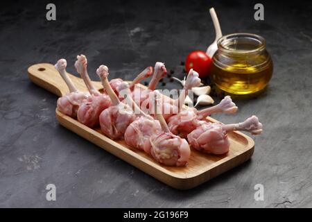 Roher Hühnerlollipop, zehn Stücke Hühnerlollipop auf einem Servierbrett mit Öl, Tomate und Knoblauch auf dem Hintergrund mit grauer strukturierter Basis angeordnet Stockfoto