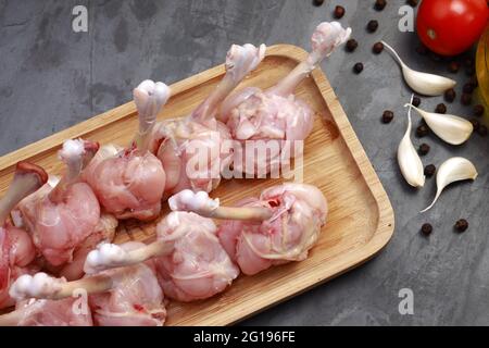 Roher Hühnerlollipop, zehn Stücke Hühnerlollipop auf einem Servierbrett mit Öl, Tomate und Knoblauch auf dem Hintergrund mit grauer strukturierter Basis angeordnet Stockfoto