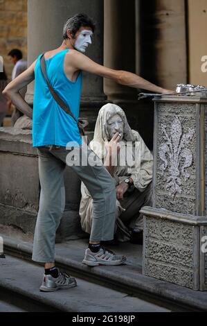 Zeit für eine Zigarettenpause Rauch, während Pantomime-Künstler in weißer Gesichtsfarbe sich von unterhaltsamen Touristen auf den Stufen der Uffizien und des Museums in den Piazzale degli Uffizien, Florenz, Toskana, Italien entspannen. Zahlreiche Maler, Künstler, Karikaturisten und Straßentheater erhalten von den Stadtverwaltungen eine Lizenz, um ihren Handel auf den Plätzen außerhalb der wichtigsten kulturellen Attraktionen der Stadt zu treiben. Stockfoto